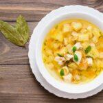 Fresh chicken broth soup with potatoes and herbs in a white bowl and bay leaf