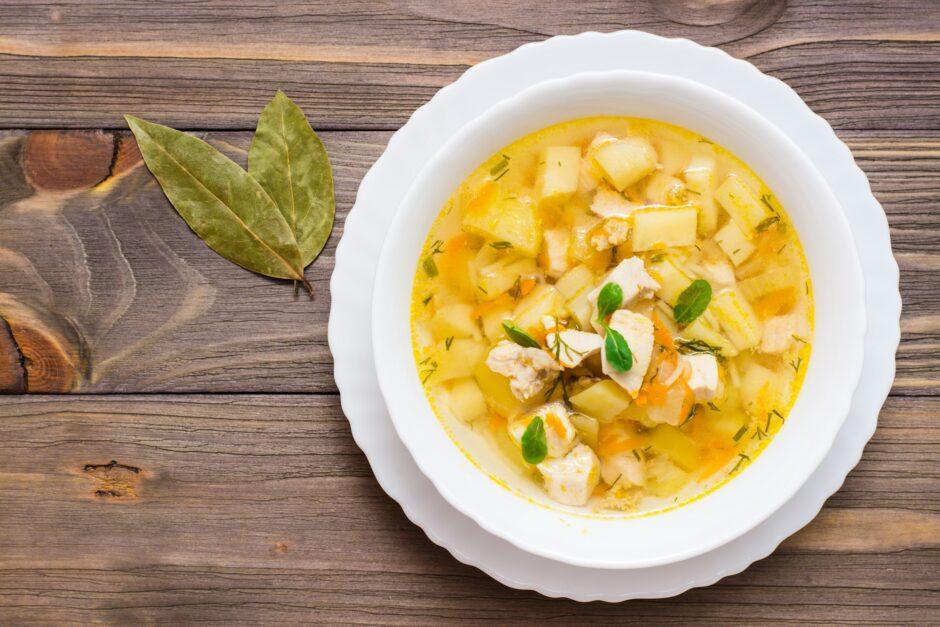 Fresh chicken broth soup with potatoes and herbs in a white bowl and bay leaf