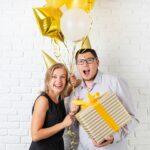 Happy young couple celebrating birthday holding a balloon and a big gift box