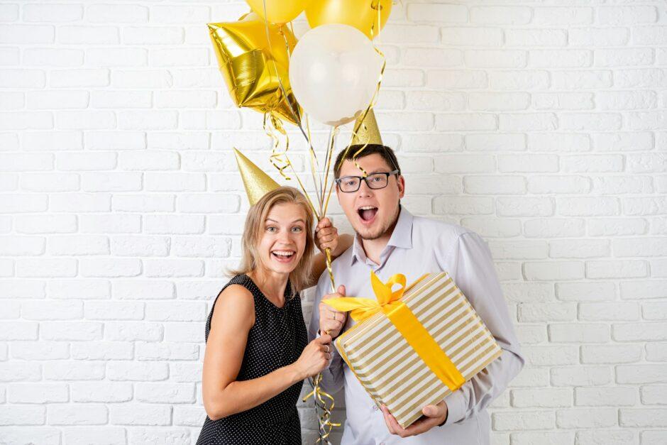 Happy young couple celebrating birthday holding a balloon and a big gift box