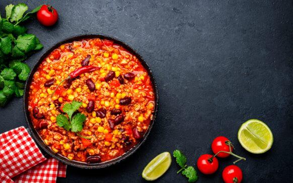 Chili con carne, mexican dish with minced beef, red beans, paprika, corn, cilantro and red peppers